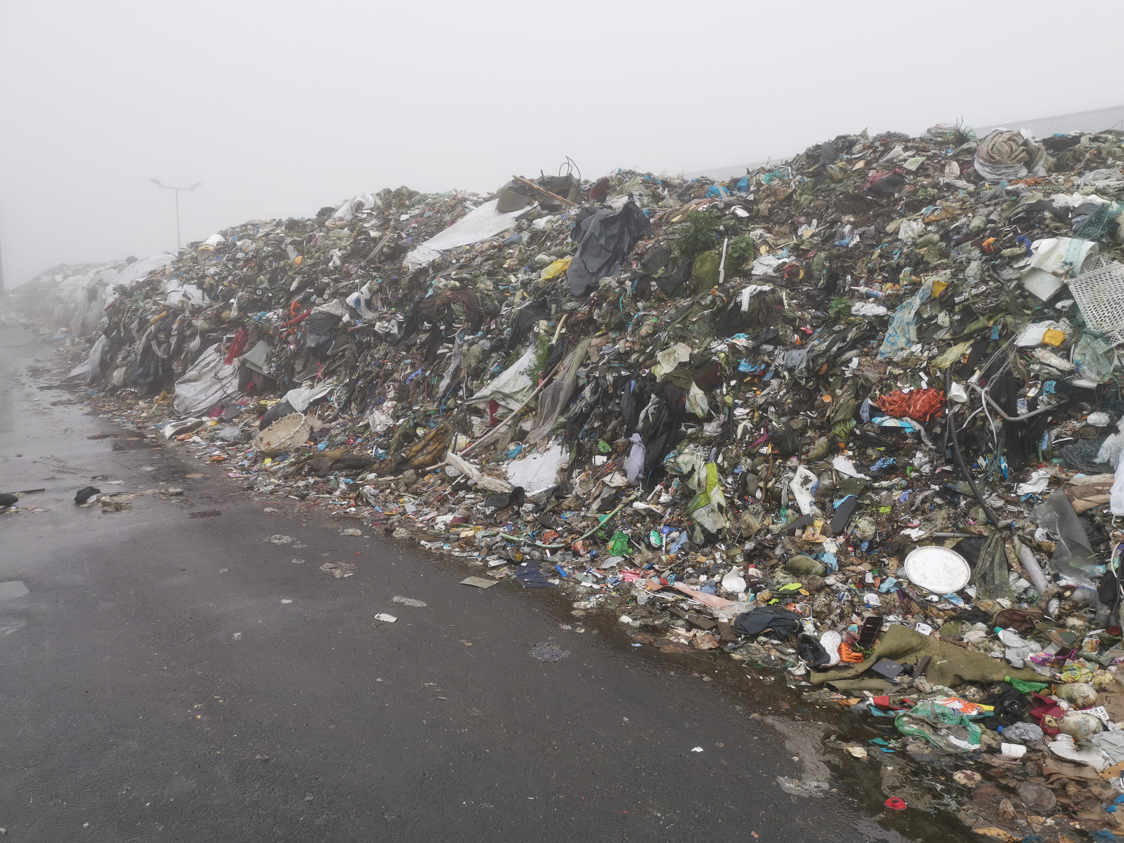 A colorful heap of landfill waste on a concrete flooring in foggy surroundings.