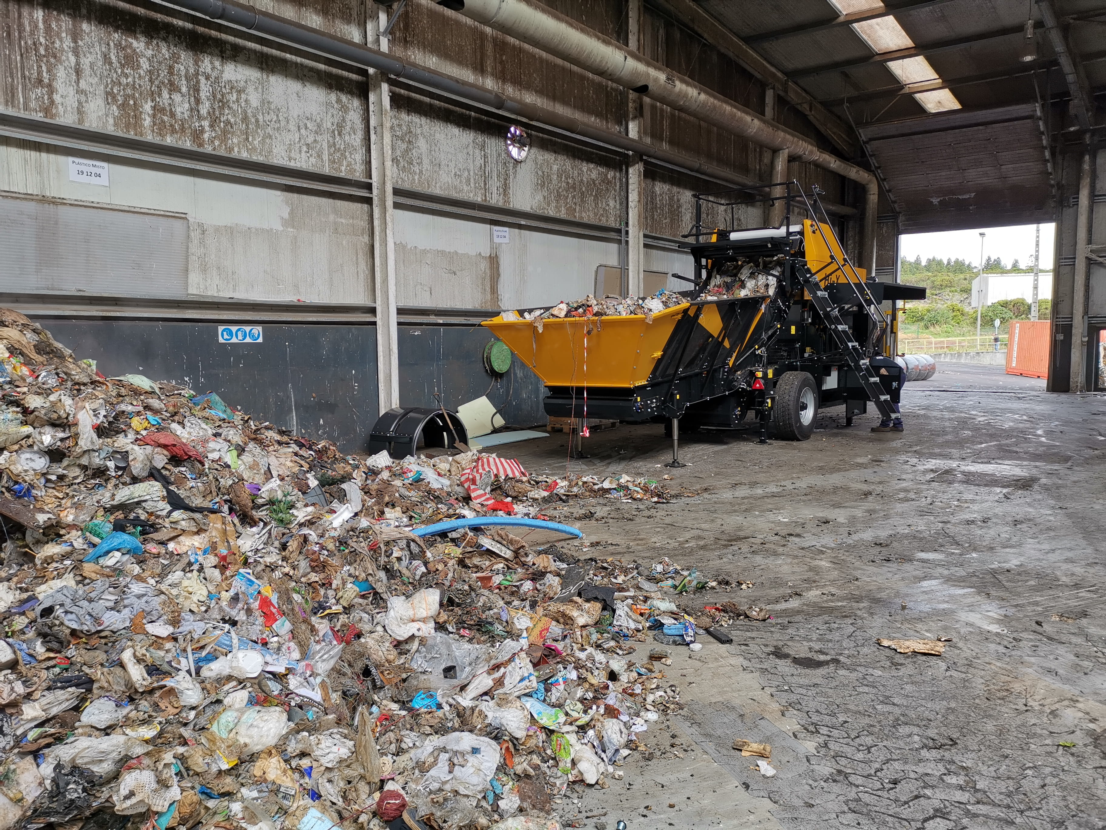 A Hi-X compactor in a concrete facility, with loose landfill waste in its feeding table and heaps of loose waste in the foreground.