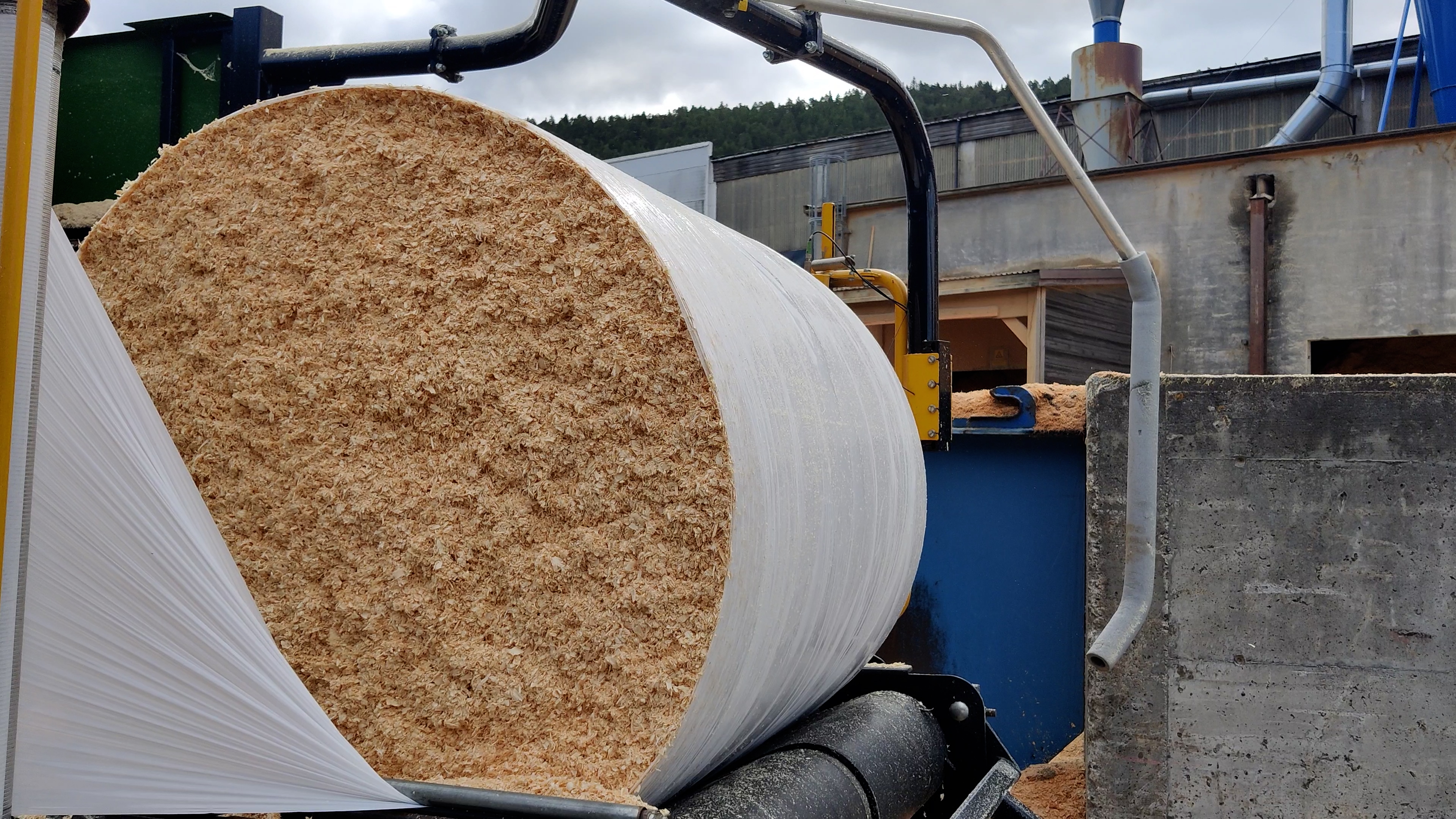 A half-wrapped wood shavings bale with the bale sides still exposing the yellow material.