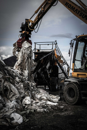 Image shows machine digging up a pile of plastic waste