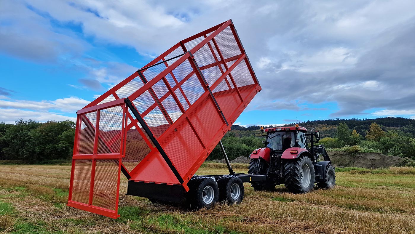 Rød Orkel TX130 traktorhenger med graspåbygg stående ute på jordet, kornstubb, trær og blå himmel i bakgrunn